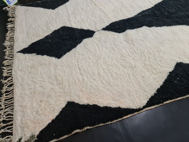May include: A white and black geometric patterned rug with a fringe border. The rug has a fluffy texture.