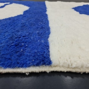 Puede incluir: Primer plano de una alfombra azul y blanca con textura peluda. La alfombra tiene un borde blanco y est&aacute; hecha de un material suave y esponjoso.