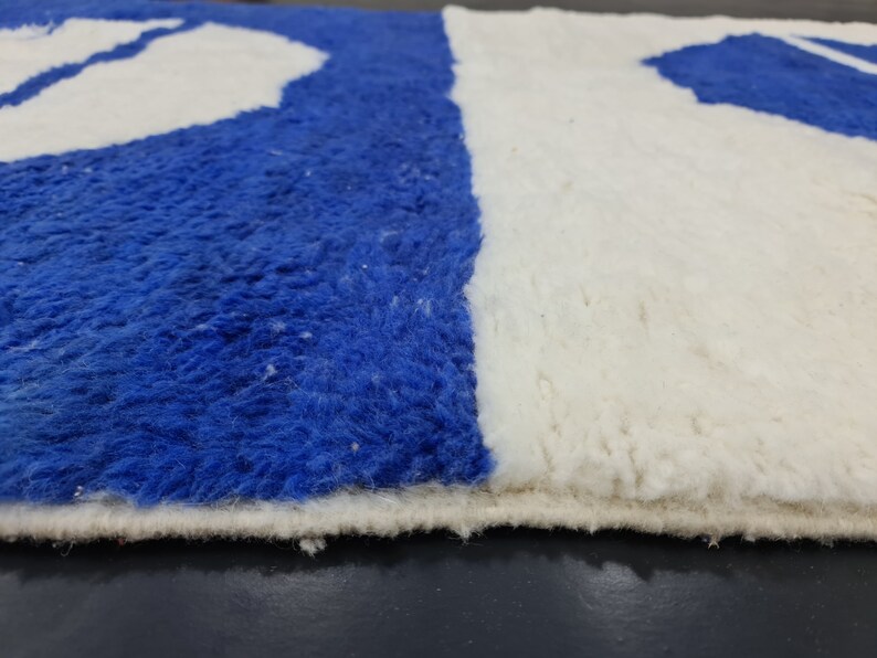 Puede incluir: Primer plano de una alfombra azul y blanca con textura peluda. La alfombra tiene un borde blanco y est&aacute; hecha de un material suave y esponjoso.