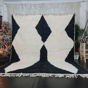 May include: A white and black Moroccan rug with a geometric pattern. The rug has a fringe border and is made of wool.