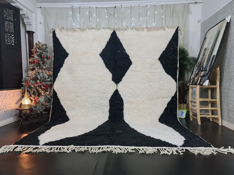 May include: A white and black Moroccan rug with a geometric pattern. The rug has a fringe border and is made of wool.