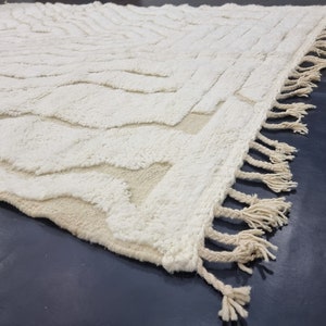 May include: A white, fluffy rug with a geometric pattern and fringe edging. The rug has a subtle, textured surface.