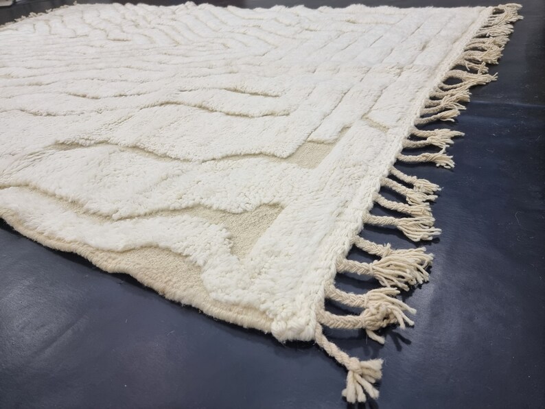 May include: A white, fluffy rug with a geometric pattern and fringe edging. The rug has a subtle, textured surface.