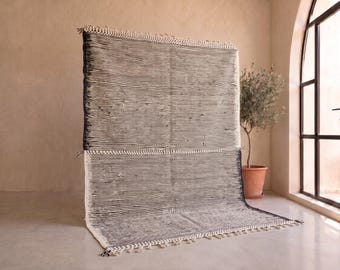May include: A large rectangular area rug featuring a dense pattern of thin horizontal black and white stripes. The rug has a textured surface with visible woven fibers and decorative fringe detailing along the top and bottom edges.