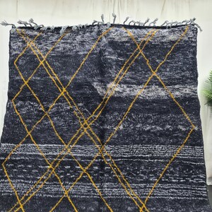 May include: A black and white rug with a geometric pattern of yellow diamonds. The rug has a fringe border.