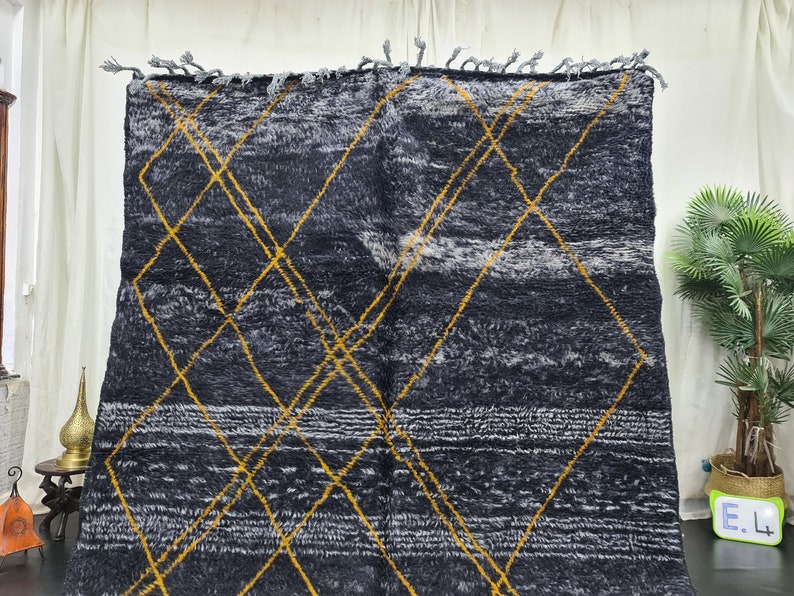 May include: A black and white rug with a geometric pattern of yellow diamonds. The rug has a fringe border.