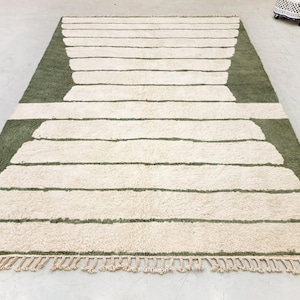 May include: A rectangular rug with a geometric design. The rug features a light green background with off-white horizontal stripes. The edges have a fringe detail. This rug is suitable for living rooms and bedrooms.