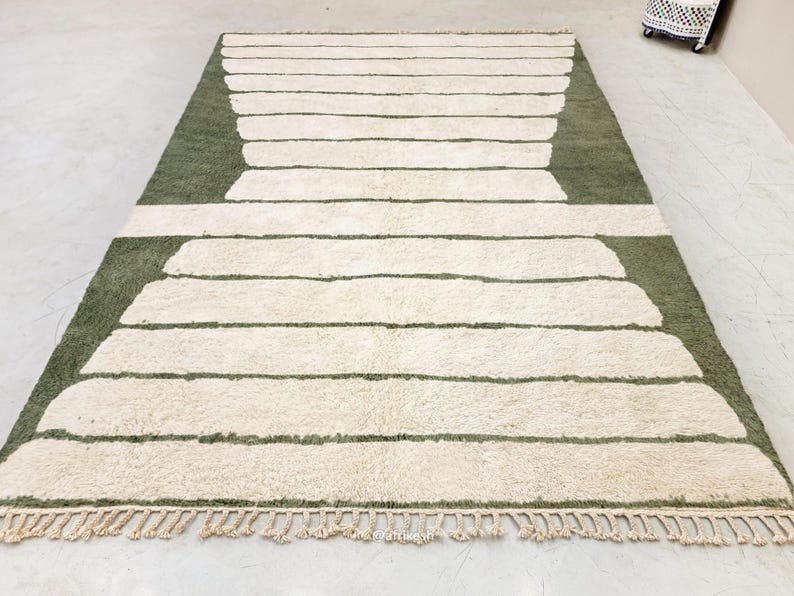 May include: A rectangular rug with a geometric design. The rug features a light green background with off-white horizontal stripes. The edges have a fringe detail. This rug is suitable for living rooms and bedrooms.