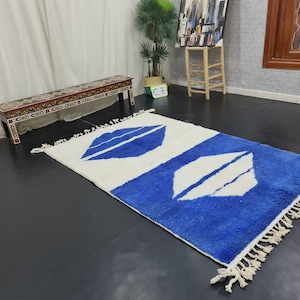 Puede incluir: Una alfombra blanca y azul con un patr&oacute;n geom&eacute;trico. La alfombra tiene un borde de flecos y est&aacute; hecha de un material suave y esponjoso.