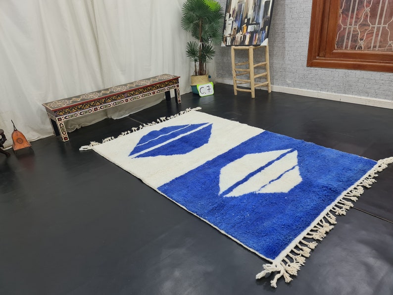 Puede incluir: Una alfombra blanca y azul con un patr&oacute;n geom&eacute;trico. La alfombra tiene un borde de flecos y est&aacute; hecha de un material suave y esponjoso.