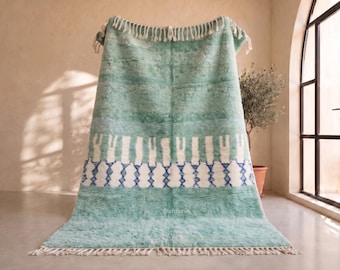 May include: A large, rectangular, mint green area rug with a high-pile texture. The rug features a horizontal band of white vertical stripes above a row of blue diamond-shaped geometric patterns. Both ends of the rug are finished with white fringe.