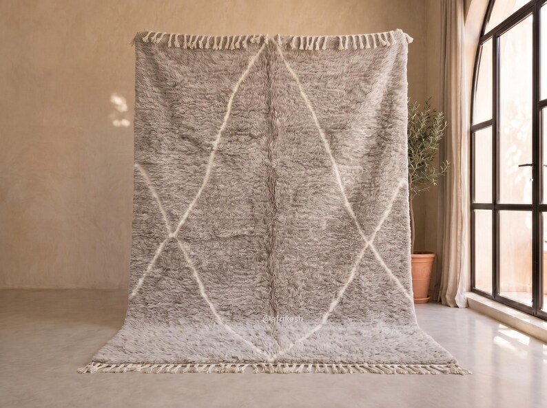 May include: A rectangular, high-pile area rug in a soft grey tone, featuring a white diamond-shaped geometric pattern across its surface. The rug is finished with short, cream-coloured fringe tassels along the top and bottom edges.