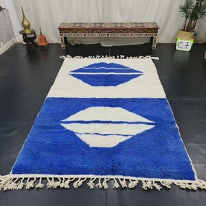 Puede incluir: Una alfombra blanca y azul con un borde de flecos. La alfombra tiene dos formas abstractas blancas que se asemejan a labios sobre un fondo azul.