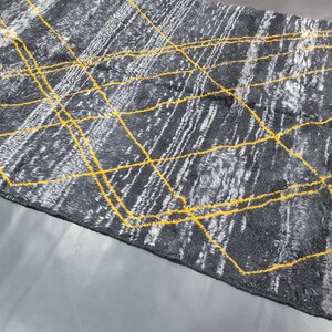 May include: A gray and white rug with a geometric pattern of yellow lines. The rug has fringe on the edges.