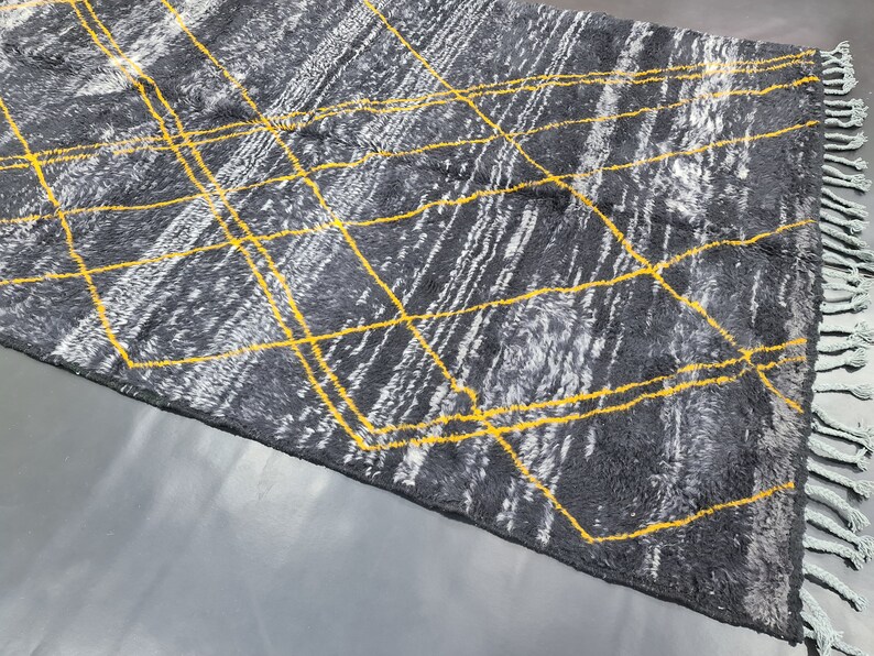 May include: A gray and white rug with a geometric pattern of yellow lines. The rug has fringe on the edges.