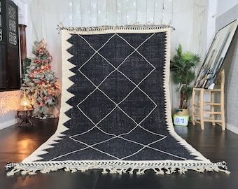 May include: Black and white Moroccan rug with a diamond pattern. The rug has a fringe border and is made of wool.