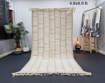 May include: A white rectangular rug with a woven pattern of squares. The rug has a fringe border and measures 4.8 x 8.9 feet.