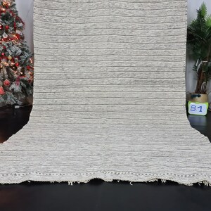 Puede incluir: Una alfombra rayada blanca y gris con un borde de flecos. La alfombra est&aacute; hecha de un material suave y texturizado.