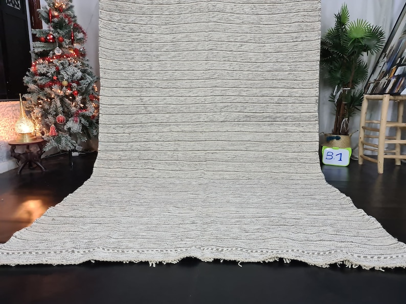 Puede incluir: Una alfombra rayada blanca y gris con un borde de flecos. La alfombra est&aacute; hecha de un material suave y texturizado.