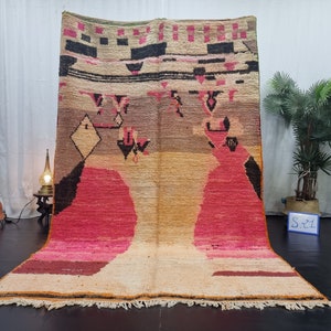 May include: A large, hand-woven rug with a geometric pattern in shades of pink, orange, brown, and black. The rug has a fringe border and is made of wool.