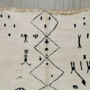 May include: A white Moroccan rug with a black geometric pattern. The pattern includes diamonds, crosses, and other abstract shapes.