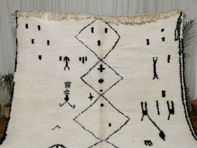 May include: A white Moroccan rug with a black geometric pattern. The pattern includes diamonds, crosses, and other abstract shapes.