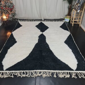 May include: Black and white rug with a geometric pattern and fringe. The rug has a modern design and is made of soft, fluffy material.