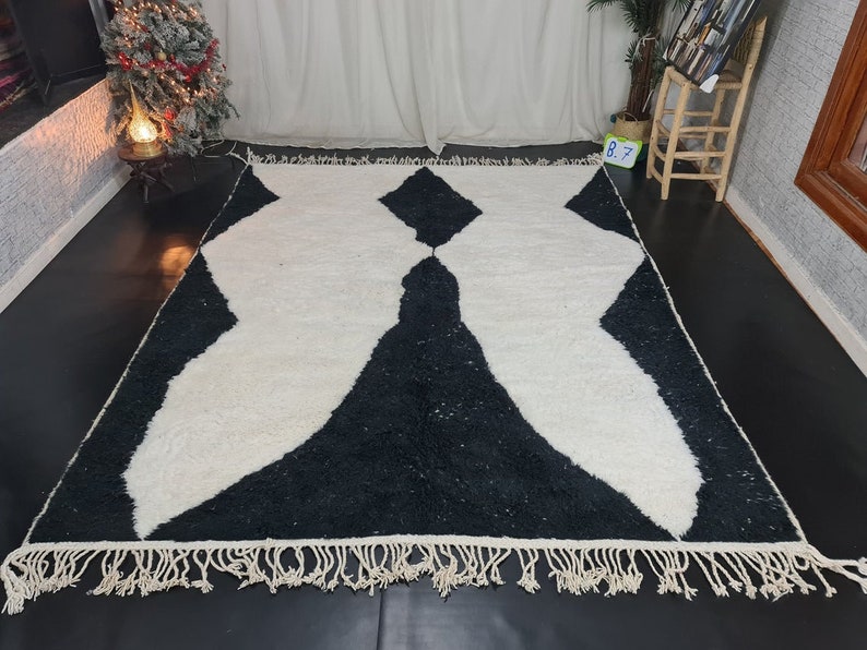 May include: Black and white rug with a geometric pattern and fringe. The rug has a modern design and is made of soft, fluffy material.