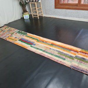 May include: A colorful, striped rug with a geometric pattern in shades of orange, red, green, blue, and pink. The rug is made of wool and has a hand-woven texture.