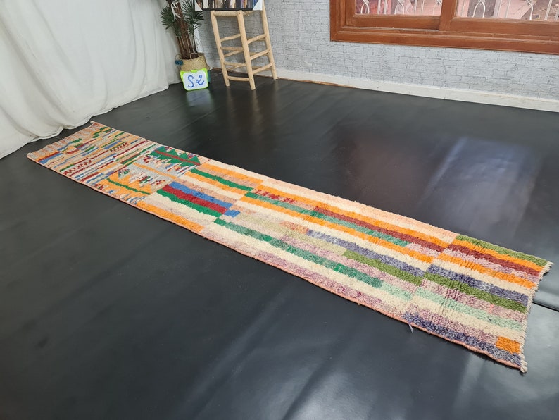 May include: A colorful, striped rug with a geometric pattern in shades of orange, red, green, blue, and pink. The rug is made of wool and has a hand-woven texture.