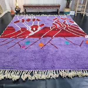 May include: A purple and red Moroccan rug with a geometric design and white fringe. The rug has a variety of colorful accents, including turquoise, pink, and orange.