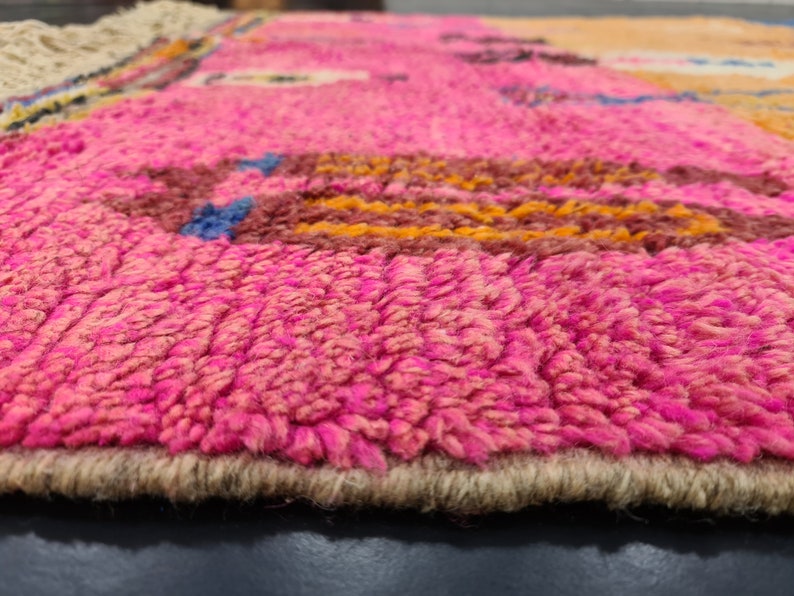 May include: Close-up of a pink and brown woven rug with a fringe border. The rug has a textured, fuzzy surface.