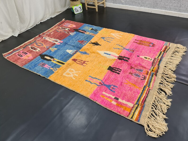 May include: A colorful Moroccan rug with a geometric pattern and fringe. The rug is made of wool and has a variety of colors, including red, blue, yellow, and pink.