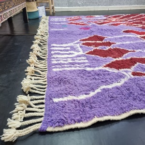May include: A purple and red patterned rug with white fringe. The rug has a fluffy texture and is made of wool.