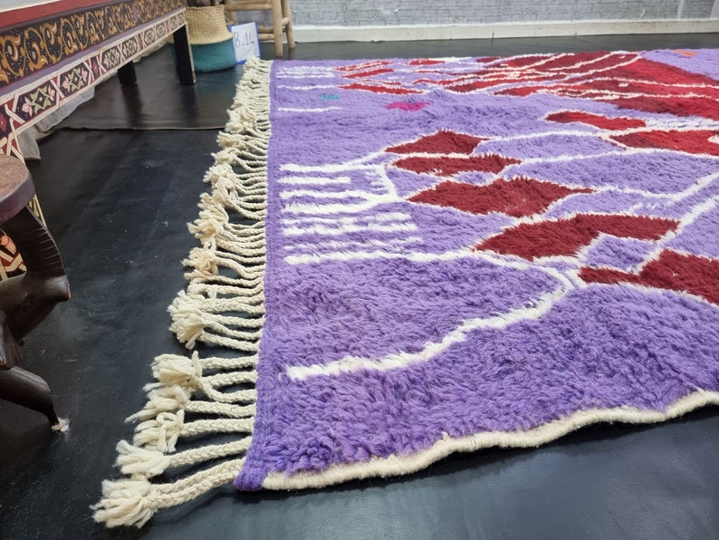 May include: A purple and red patterned rug with white fringe. The rug has a fluffy texture and is made of wool.