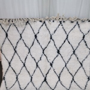 May include: White and black Moroccan rug with a diamond pattern. The rug has a fringe border.