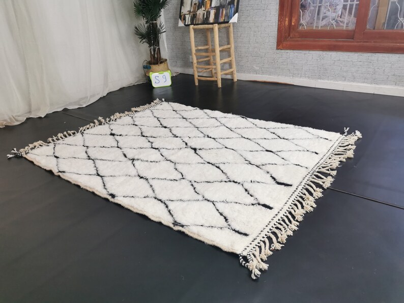 May include: A white and black diamond patterned rug with fringe. The rug is made of a soft, fluffy material.