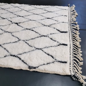 May include: A white and black Moroccan rug with a diamond pattern and fringe on the edges.