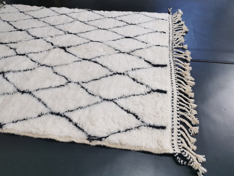 May include: A white and black Moroccan rug with a diamond pattern and fringe on the edges.