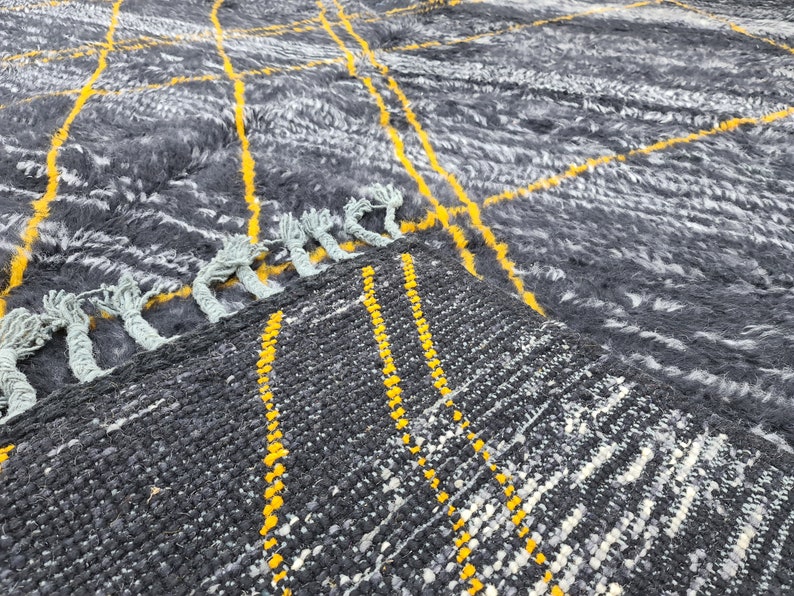 May include: Close-up of a gray and white woven rug with yellow stripes. The rug has a fringe border.