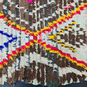 May include: A colorful woven rug with a geometric pattern. The rug is made with a variety of colors, including red, yellow, blue, and white. The rug has a fringe border.