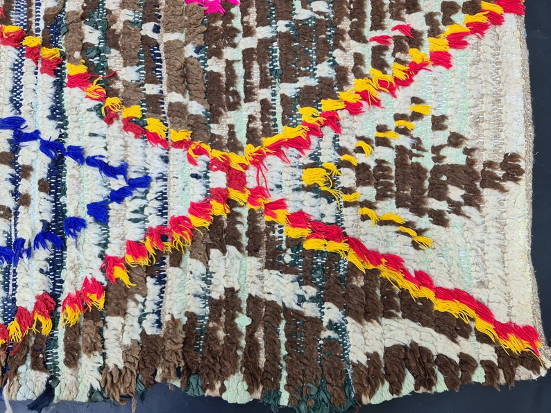 May include: A colorful woven rug with a geometric pattern. The rug is made with a variety of colors, including red, yellow, blue, and white. The rug has a fringe border.