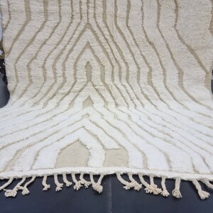 May include: A white and cream colored rug with a geometric pattern. The rug has a fringe border.