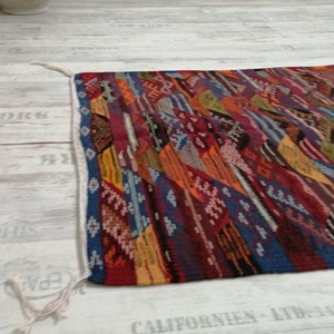 Pu&ograve; includere: Un tappeto rettangolare colorato con un design patchwork. Il tappeto presenta una variet&agrave; di colori tra cui rosso, blu, arancione e giallo. I bordi sono rifiniti con un bordo blu e frange bianche.