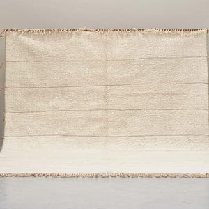 May include: A white woven rug with a fringe border. The rug has a subtle texture and a simple design.