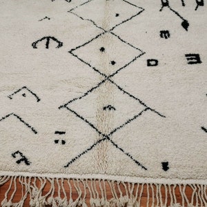 May include: A white rug with a black geometric pattern. The rug has a fringe border.