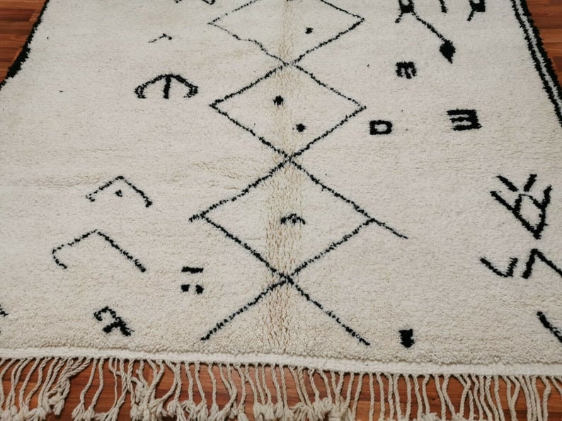 May include: A white rug with a black geometric pattern. The rug has a fringe border.