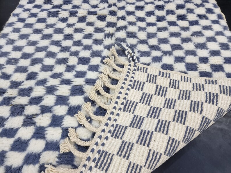 Op de afbeelding: Een blauw en wit geruit tapijt met een franje rand. Het tapijt is gemaakt van een zacht, pluche materiaal.