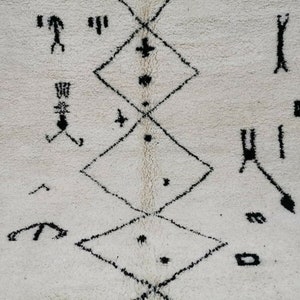 May include: A white rug with a black geometric pattern. The pattern is made up of diamonds and other shapes. The rug is made of wool and has a soft texture.