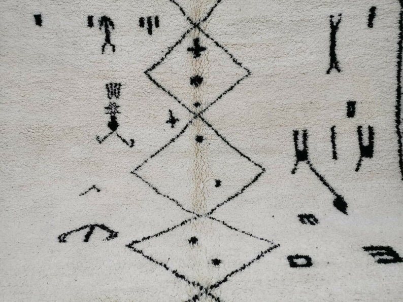 May include: A white rug with a black geometric pattern. The pattern is made up of diamonds and other shapes. The rug is made of wool and has a soft texture.
